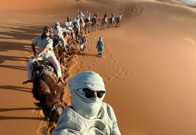 Tourists riding camels in Merzouga Desert Tourists riding camels on sand dunes
Tourists enjoying a camel trek on sand dunes in Merzouga.